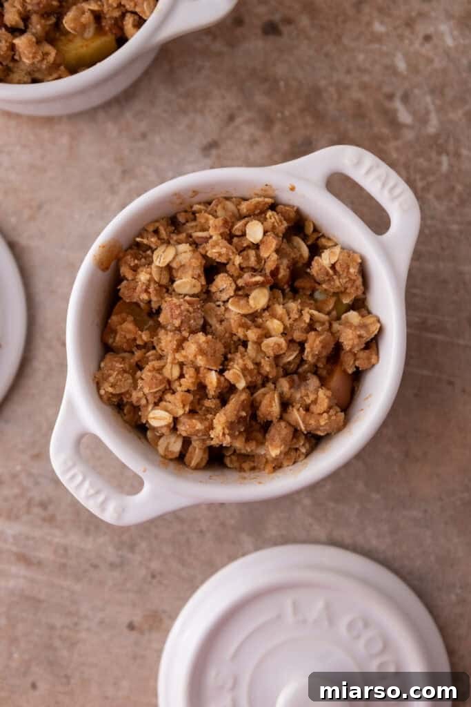 Prepared crisp topping evenly spread over the apple filling in a mug, ready for the microwave.