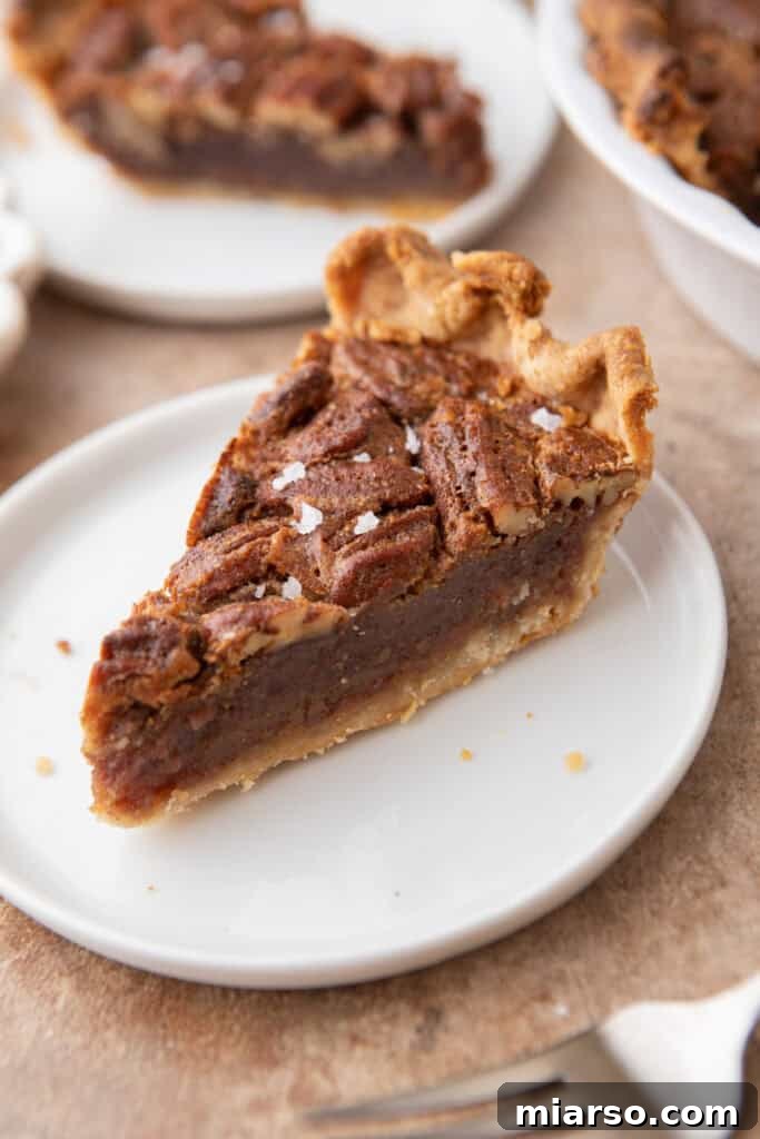 A perfectly baked slice of maple pecan pie on a white plate, showcasing its golden crust and rich, nutty filling.