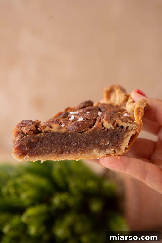 A beautiful side shot of a fully baked maple pecan pie, highlighting its impressive height, the flaky texture of the crust, and the rich, glistening layers of the pecan and maple filling.