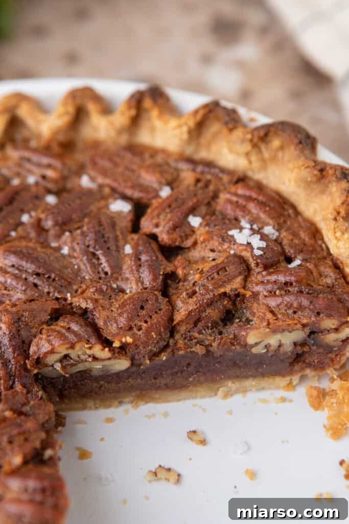 A perfectly baked maple pecan pie with a single slice removed, revealing the rich, gooey, and nutty filling encased in a flaky, golden-brown crust.