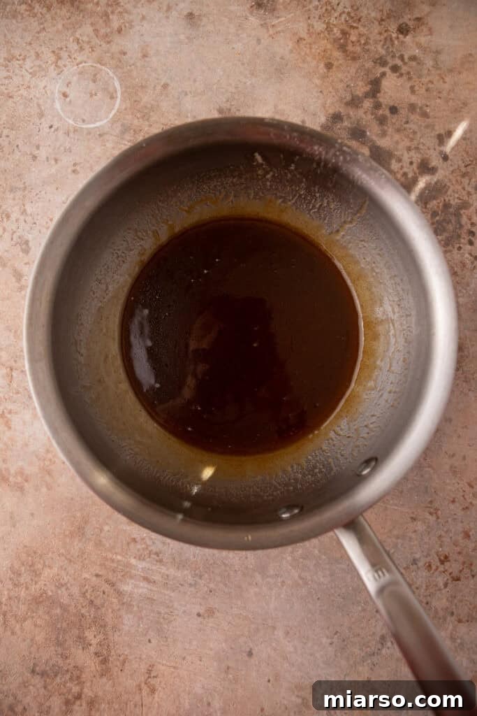 Unsalted butter browning in a saucepan over a stove, turning a rich golden color and emitting a nutty aroma, a crucial step for flavor development in the pie filling.