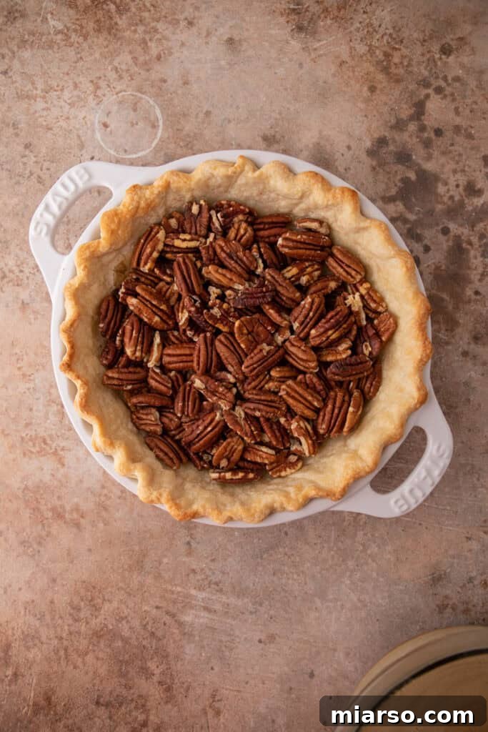 Finely chopped pecans evenly scattered across the bottom of an unbaked pie crust, forming a crunchy layer before the maple filling is added.