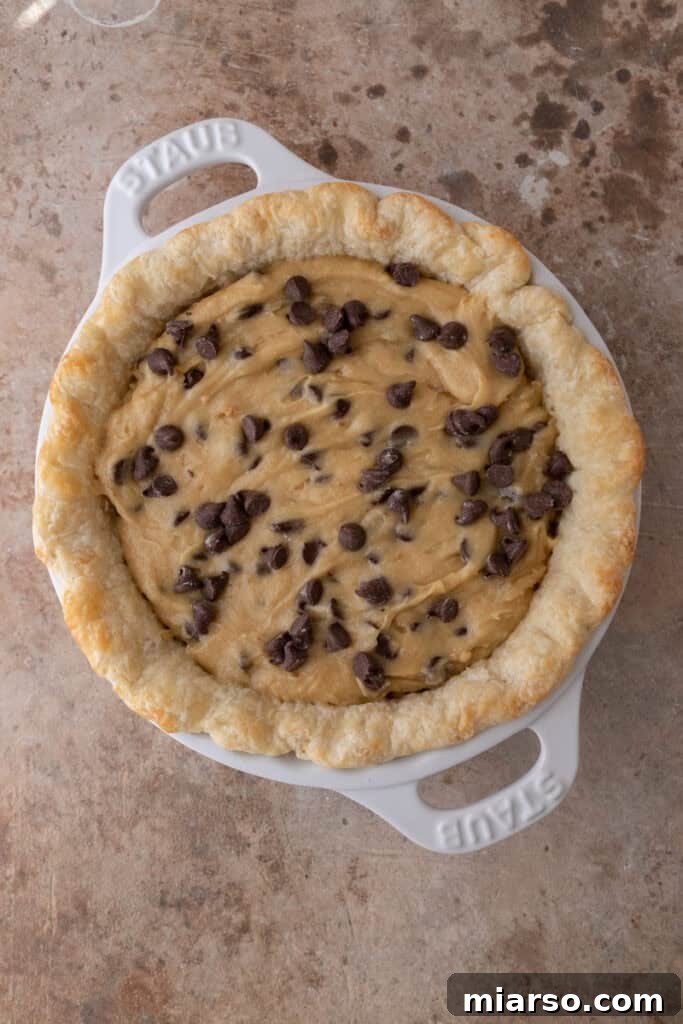 raw chocolate chip cookie pie batter spread evenly in an unbaked pie crust