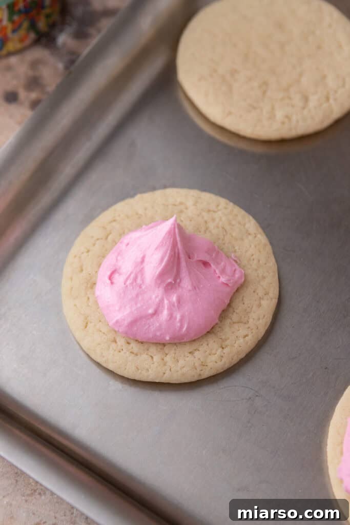 Soft and Fluffy Sour Cream Sugar Cookies 11 A freshly baked, cooled sour cream sugar cookie topped with a generous spoonful of fluffy pink frosting, ready to be smoothly spread across its surface.