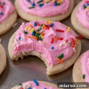 Soft sour cream sugar cookie with pink frosting and rainbow sprinkles, with a bite taken out to show the tender interior.