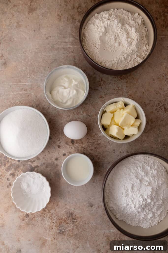 Soft and Fluffy Sour Cream Sugar Cookies 3 Neatly arranged ingredients for making sour cream sugar cookies on a rustic wooden table. The display includes all-purpose flour, granulated sugar, softened unsalted butter, a fresh large egg, creamy sour cream, and a bottle of vanilla extract, all ready for baking.