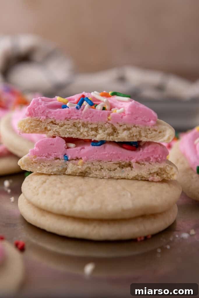 Soft and Fluffy Sour Cream Sugar Cookies 4 A stack of perfectly baked soft sour cream sugar cookies, with one cookie cut open to reveal its fluffy, airy interior and inviting texture. Some cookies are frosted with a smooth white icing.
