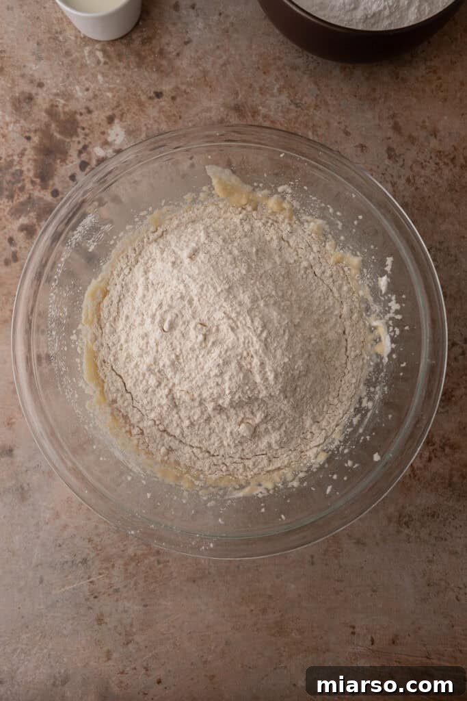 Soft and Fluffy Sour Cream Sugar Cookies 6 The pre-whisked flour mixture, including baking powder, baking soda, and salt, being carefully added in stages to the rich, creamy wet ingredients in a mixing bowl, ensuring proper incorporation without overmixing.