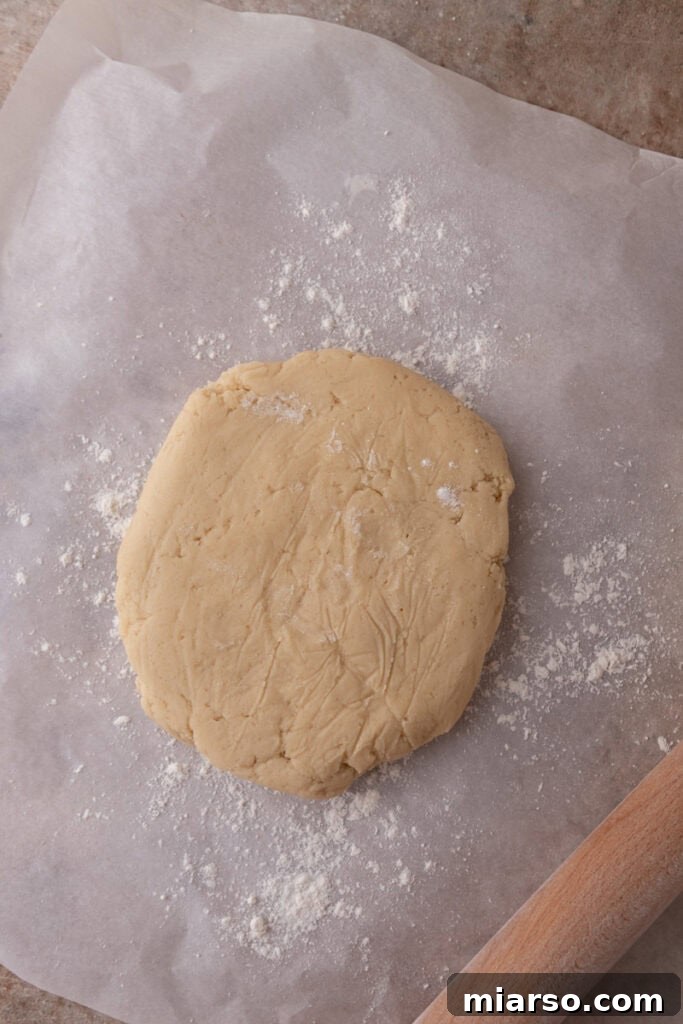 Soft and Fluffy Sour Cream Sugar Cookies 8 A disc of unbaked sour cream sugar cookie dough, thick and uniform, positioned on parchment paper, awaiting its chilling process before being rolled out and cut.