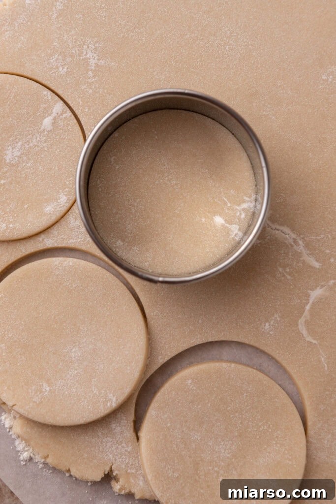 Soft and Fluffy Sour Cream Sugar Cookies 9 Smoothly rolled-out sour cream sugar cookie dough covering a surface, with a classic round cookie cutter in the process of pressing out perfect circular shapes from the dough.