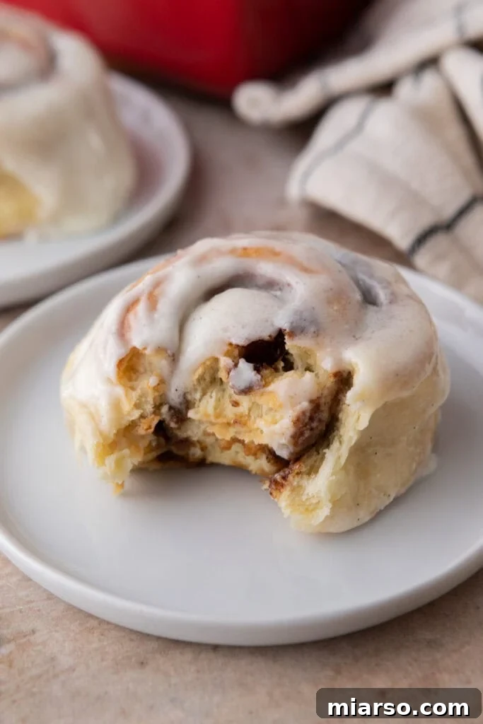 Perfect Small Batch Cinnamon Rolls 2 Soft small batch cinnamon roll with a bite taken out, showing fluffy layers and cinnamon filling, topped with vanilla frosting.