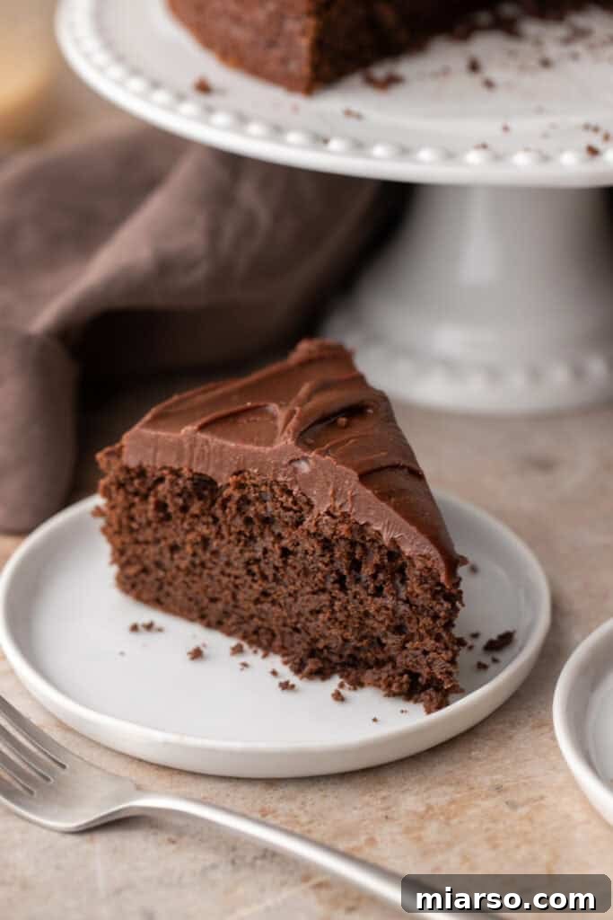 A delectable slice of Sourdough Discard Chocolate Cake resting on a pristine white plate, showcasing its moist crumb and glossy ganache frosting.