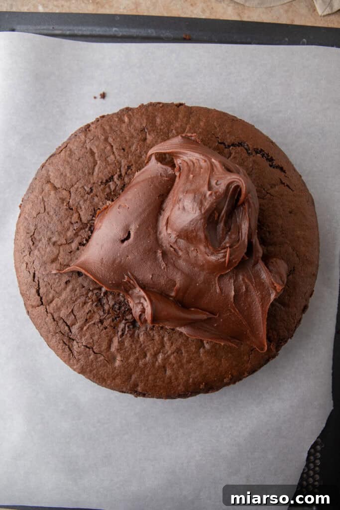 A smooth, glossy chocolate ganache being spread meticulously over the top of the cooled sourdough chocolate cake.