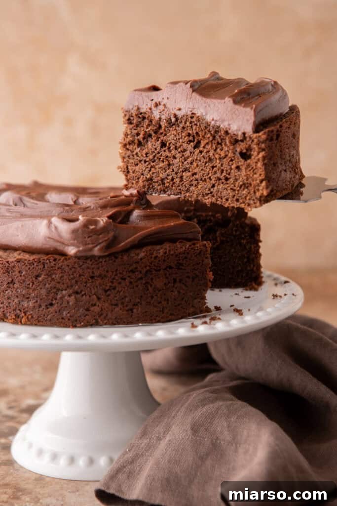 A hand gently removing a perfect slice of Sourdough Discard Chocolate Cake from the full cake, revealing its moist interior.