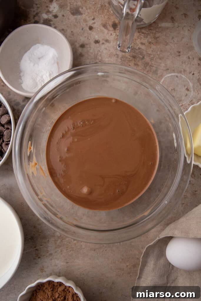 Wet ingredients including eggs and vanilla extract being whisked into the melted chocolate mixture.