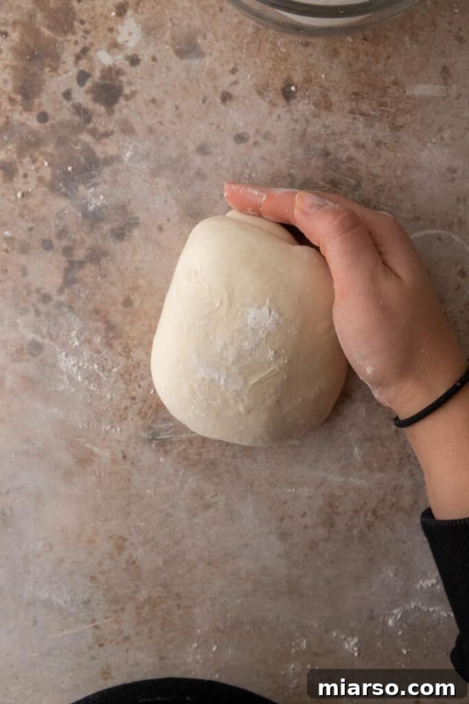 stretched out dough folded on a floured surface and rolled into a ball