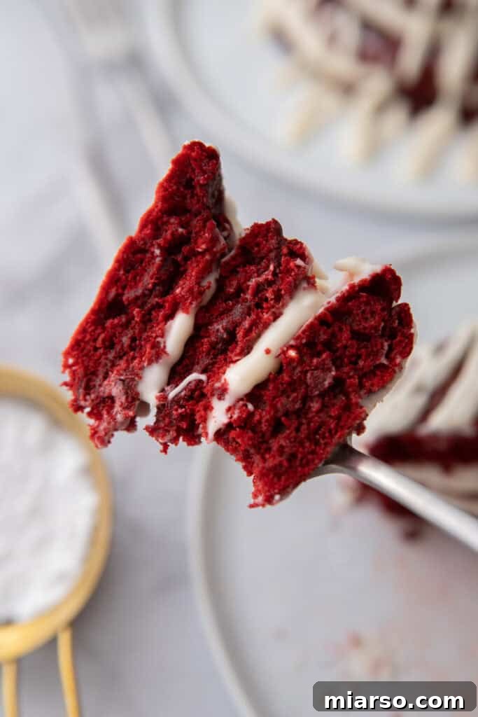 Indulgent Red Velvet Pancakes 12 A close-up of a Red Velvet Pancake being held by a fork, showcasing its intricate layers and cream cheese glaze, inviting a taste.