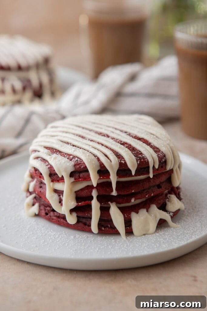 Indulgent Red Velvet Pancakes 9 Another enticing shot of stacked Red Velvet Pancakes, glistening with cream cheese glaze and powdered sugar, emphasizing their inviting texture.
