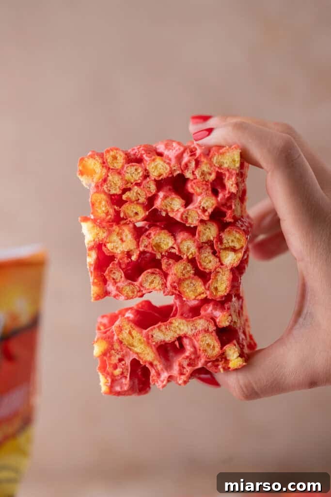 A hand holding a piece of Hot Cheetos Marshmallow Crispy Treat, showing its vivid color and texture.