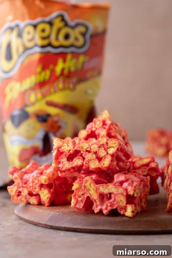 Three Hot Cheetos Marshmallow Crispy Treats stacked on a marble surface, highlighting their fiery red color.