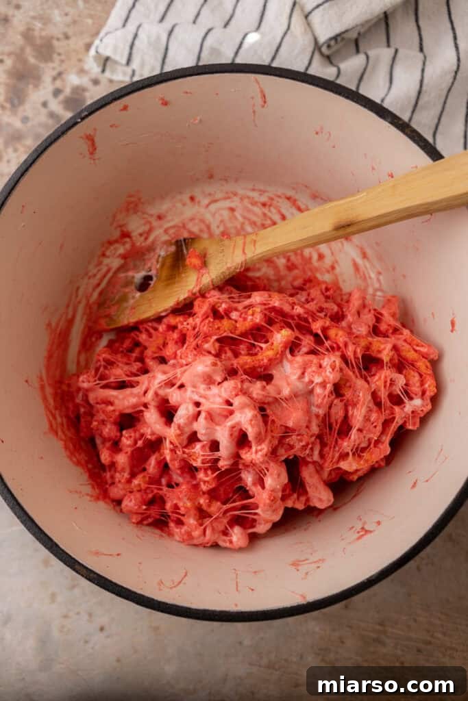 Hot Cheetos being stirred into the melted marshmallow mixture in a pot.