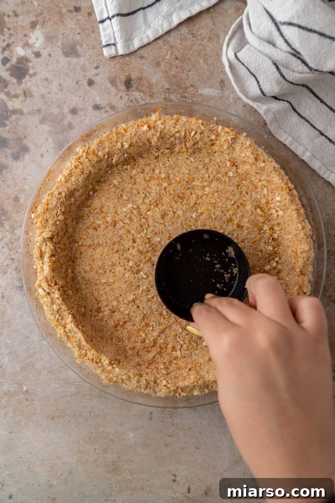 Ultimate Pretzel Pie Crust 8 Pretzel crumb mixture being firmly pressed into a pie pan.