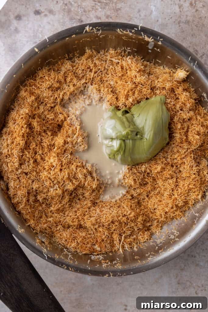 Pistachio cream, tahini, and toasted kataifi being mixed in a bowl to form the middle layer.