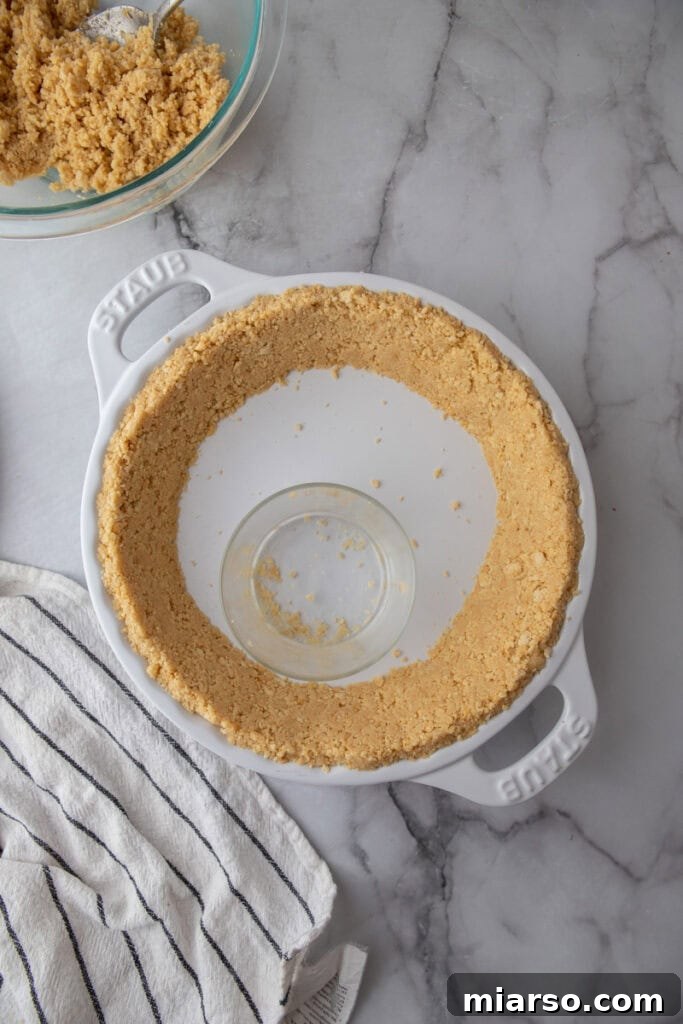 Golden Oreo Pie Crust Perfection 12 A hand gently pressing golden Oreo crumbs into the bottom of a pie pan to form an even, compact crust.