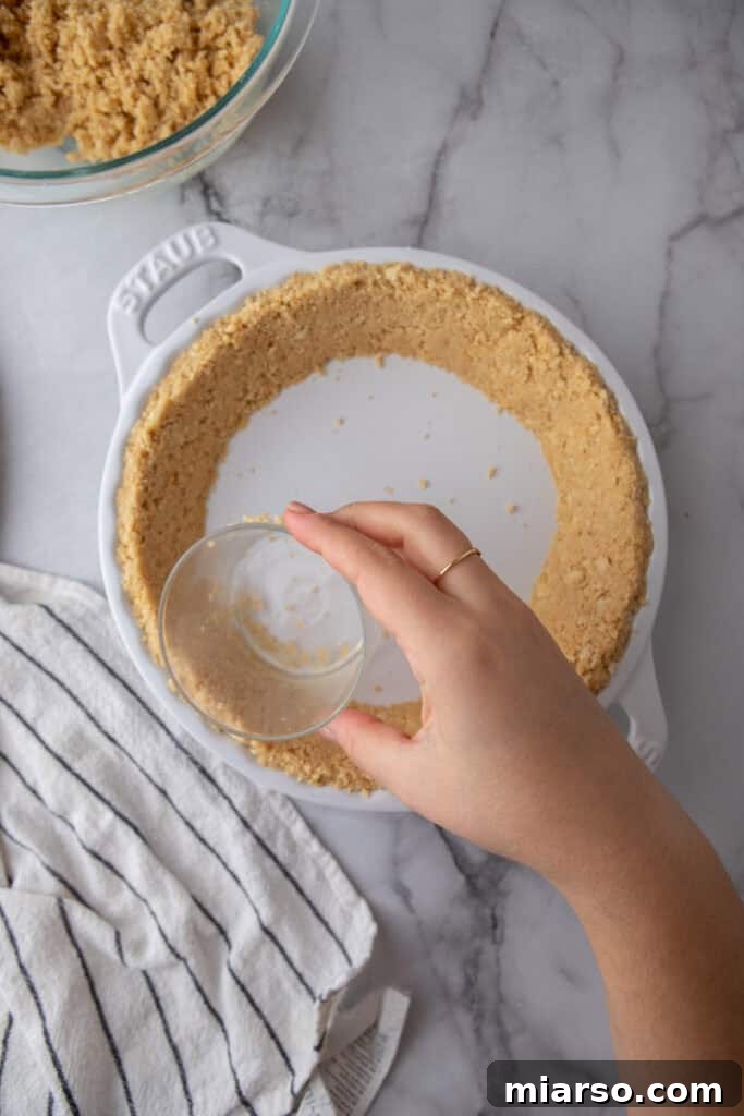 Golden Oreo Pie Crust Perfection 7 Golden Oreo crumbs being pressed firmly into a pie pan, forming the crust base.