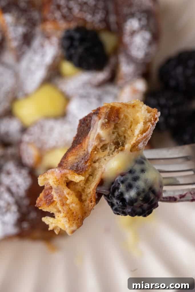 A close-up shot of a piece of Pretzel French Toast Bake being lifted on a fork, clearly showing its delectable texture, golden crust, and inviting interior.