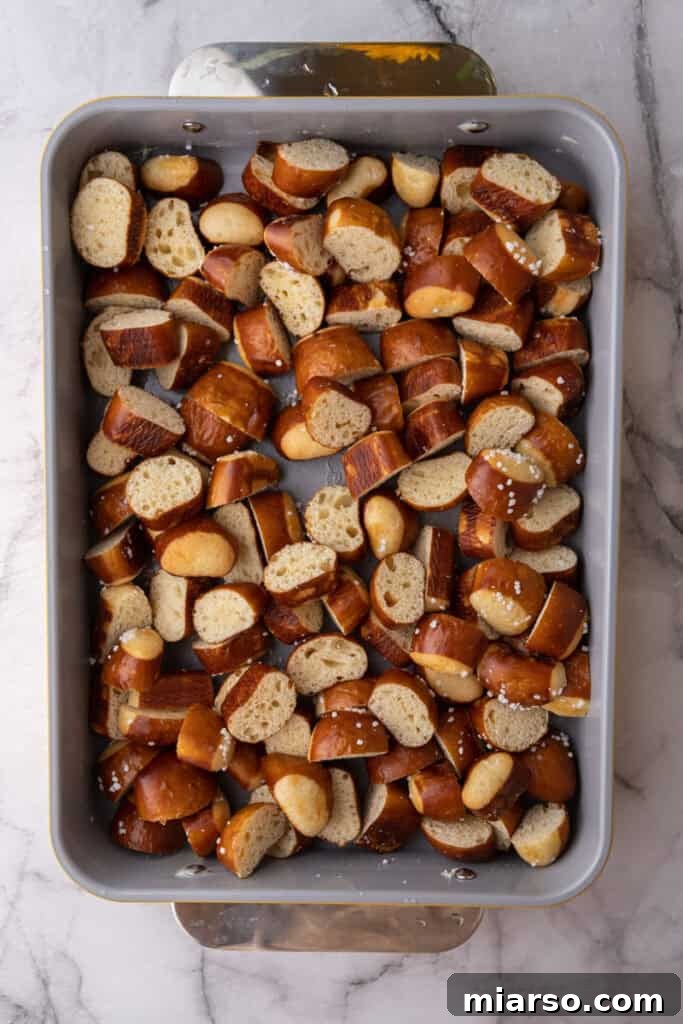 Close-up shot of perfectly cubed pretzel bread pieces arranged neatly in a buttered baking dish, forming the base of the casserole.