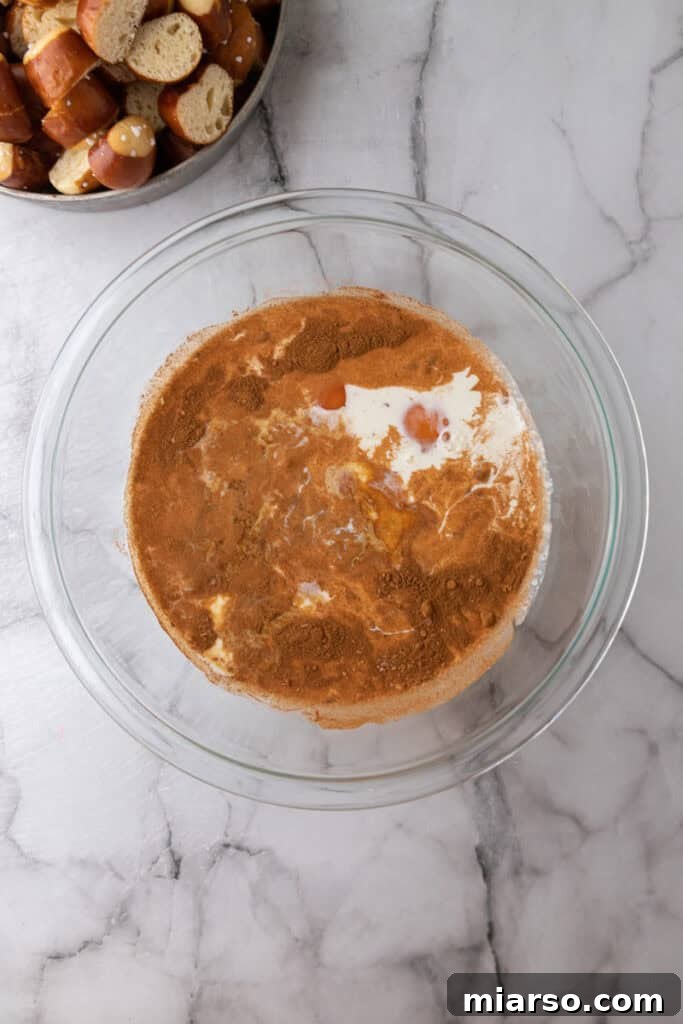 A clear glass bowl holding the unmixed wet ingredients for the custard (eggs, milk, heavy cream) before they are whisked together.