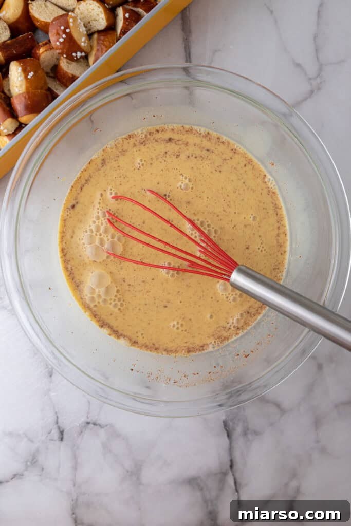 A bowl containing the smoothly whisked custard mixture, now perfectly combined and ready to be poured over the cubed pretzel bread.