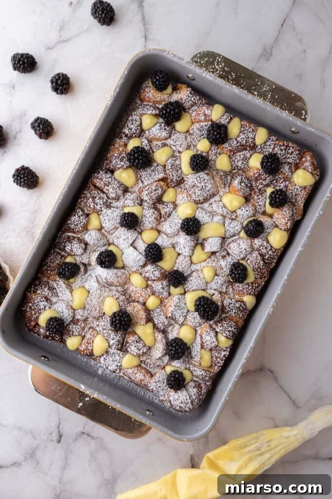A close-up of the fully cooked Pretzel French Toast Bake, elegantly dusted with powdered sugar and adorned with vibrant fresh berries and a dollop of lemon curd, ready for serving.