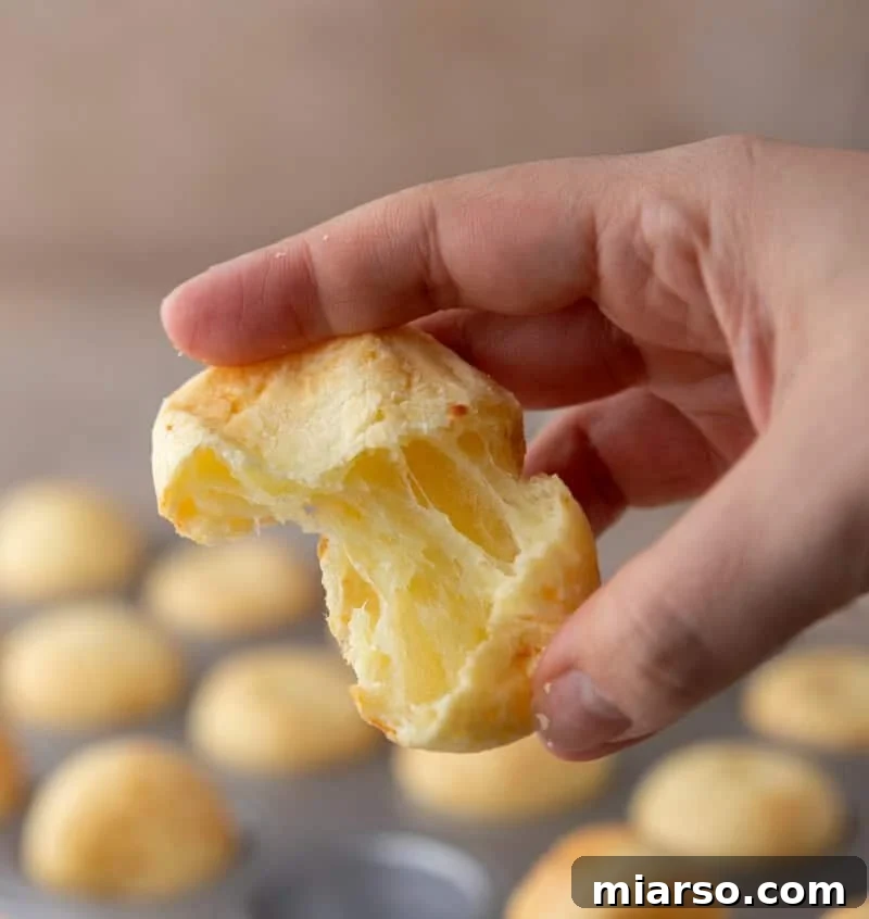 A freshly baked Brazilian cheese bread bite, torn open to reveal its signature hollow and chewy interior, showcasing the perfect texture.