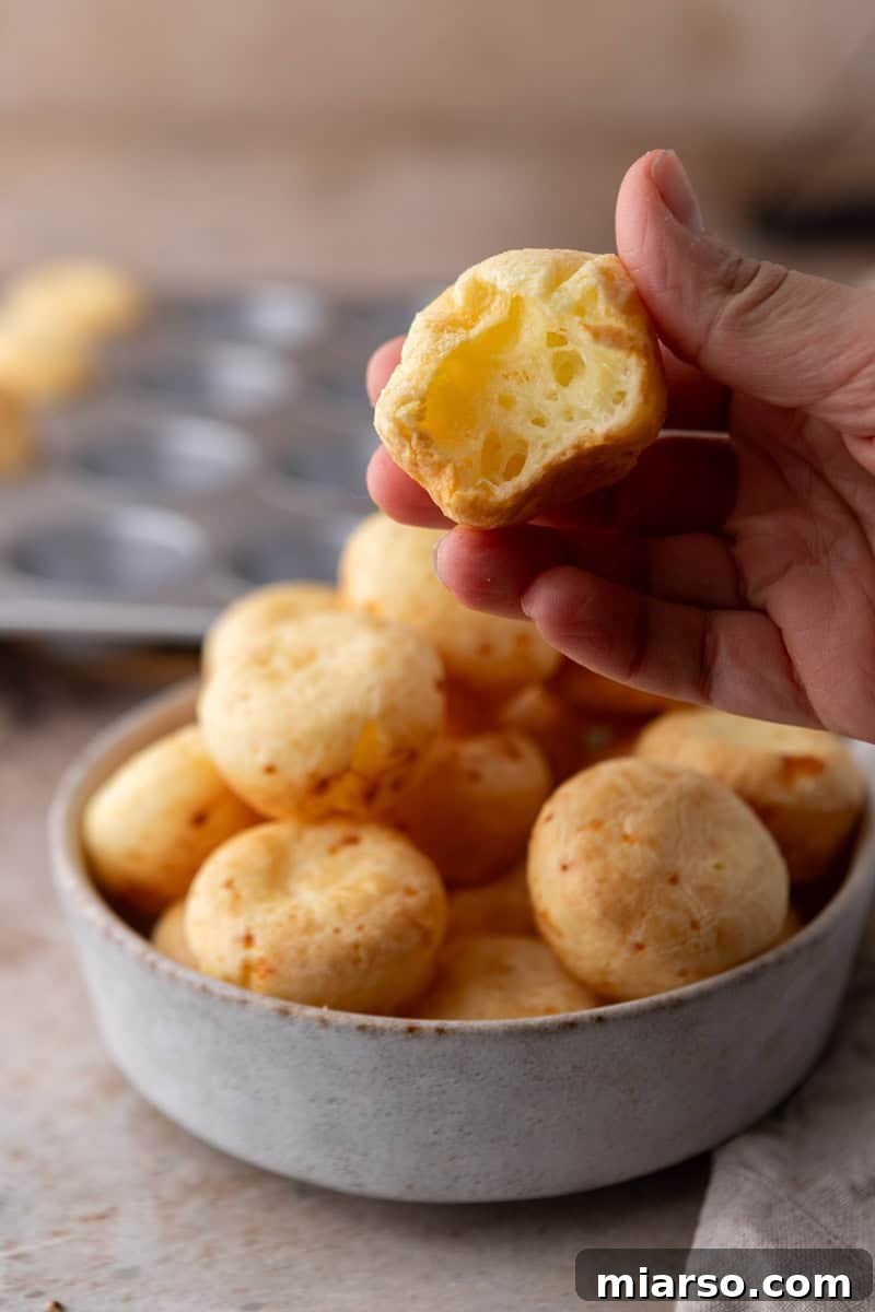 A close-up of a Brazilian cheese bread bite, perfectly golden, torn open to reveal its fluffy, hollow, and incredibly chewy interior texture.