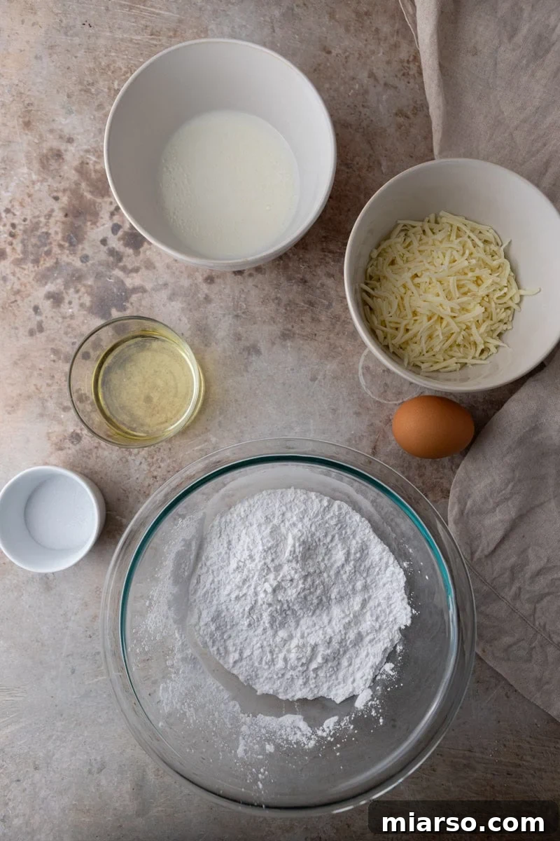 Various ingredients laid out for making Brazilian cheese bread, including tapioca flour, milk, egg, and two types of grated cheese.