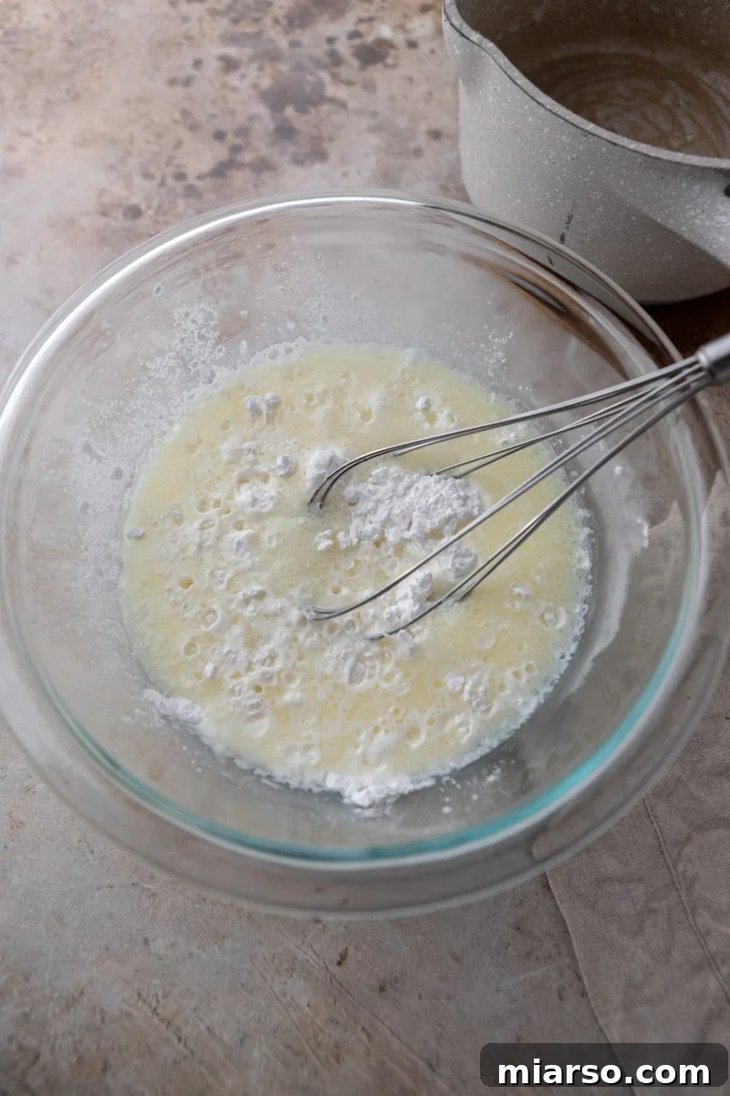 Hot milk mixture being carefully poured over tapioca flour in a mixing bowl, ready to be stirred into a thick dough.