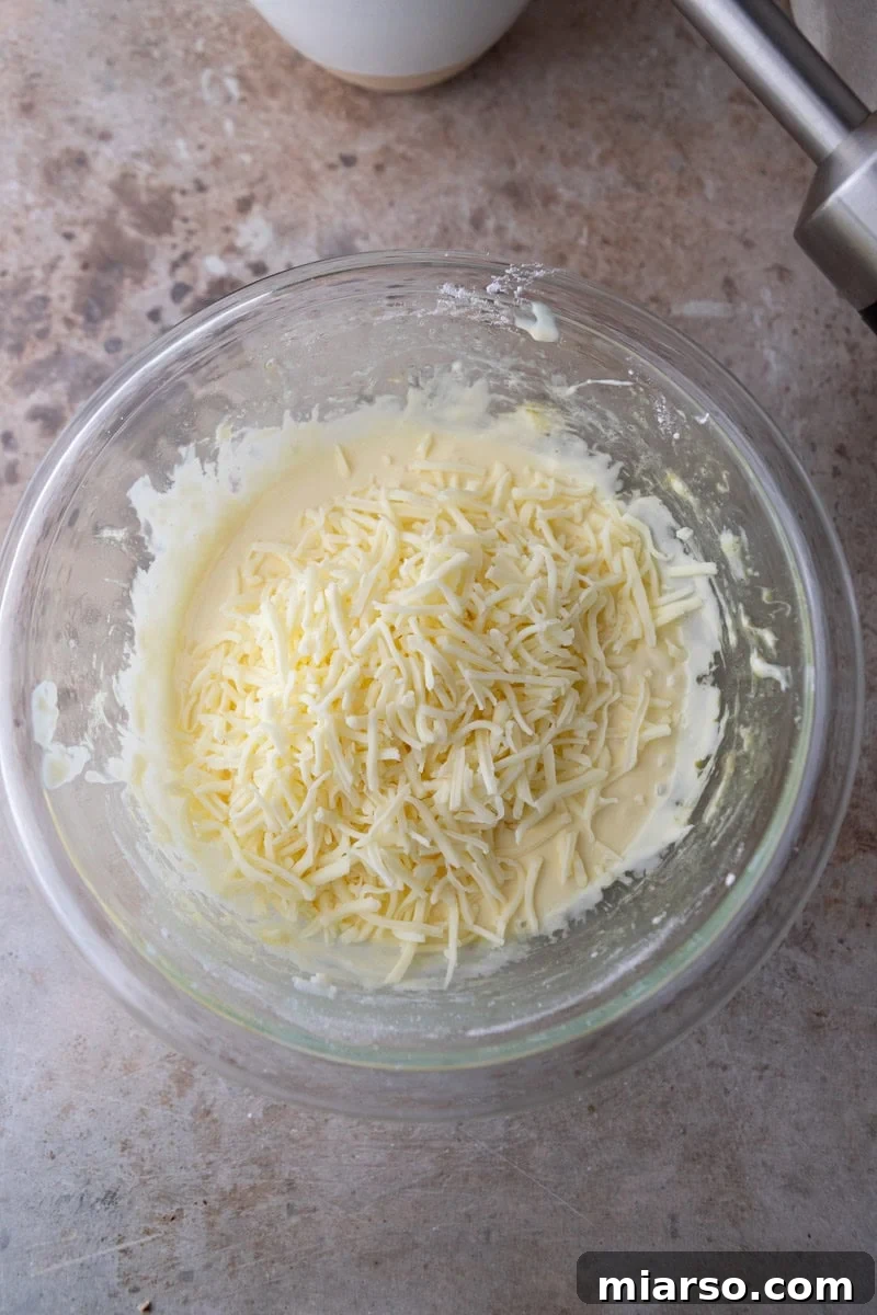 Finely grated cheese being folded into the stretchy tapioca dough, ensuring even distribution for flavorful cheese bread bites.