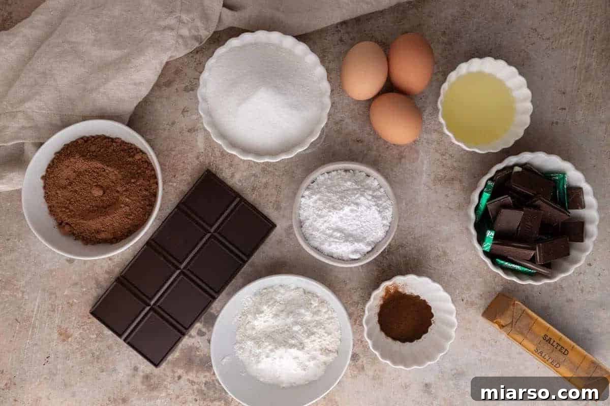 Ultra Fudgy Crinkled Andes Mint Brownies 3 Brownie ingredients arranged on a countertop including cocoa powder, eggs, flour, and chocolate, ready for baking.