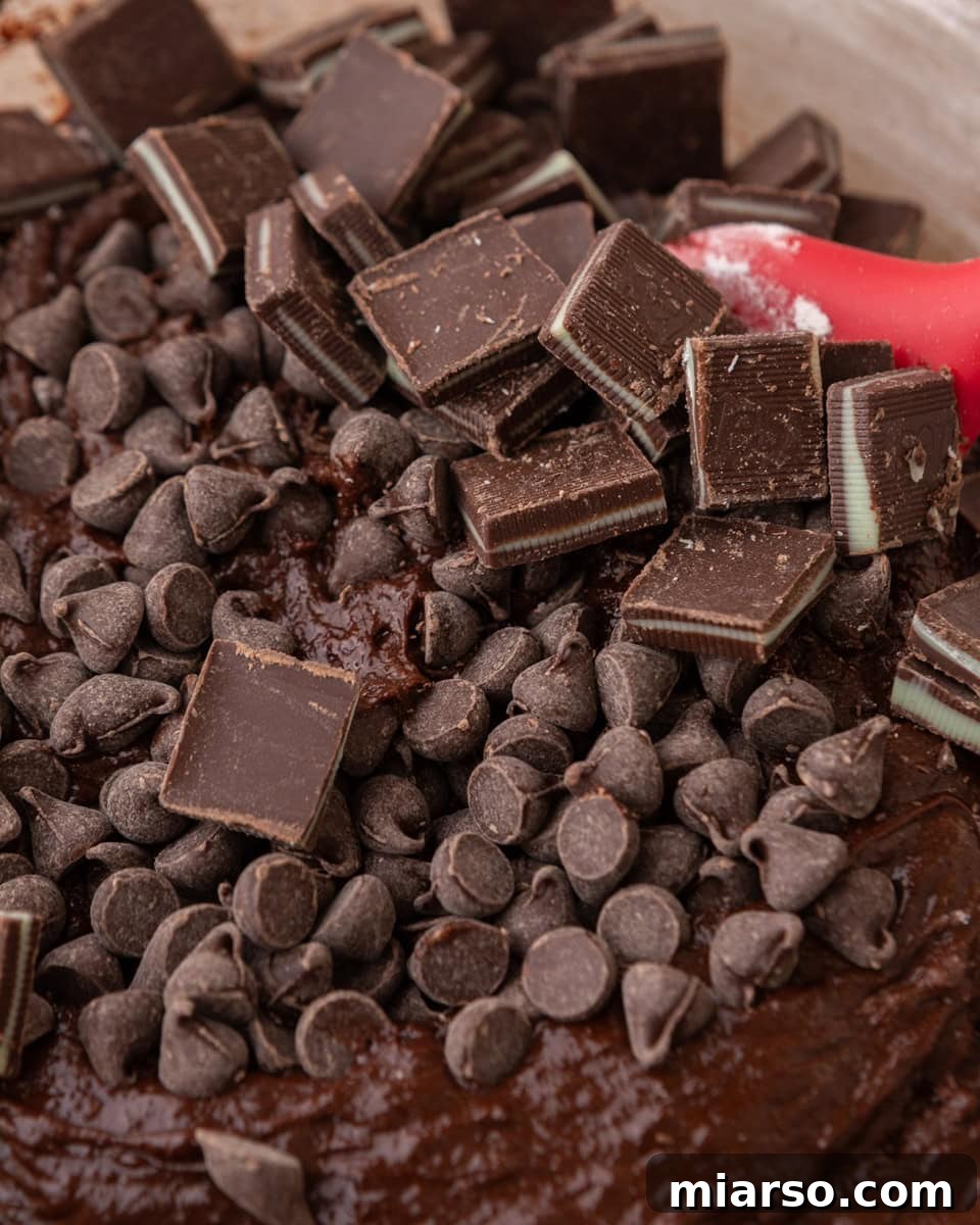 Ultra Fudgy Crinkled Andes Mint Brownies 8 Chocolate chips and chopped mint chocolate candies being mixed into brownie batter, showing the rich texture.