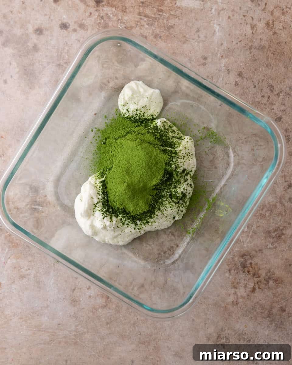A bowl with green matcha powder being whisked into creamy white Greek yogurt, showing the initial mixing step for matcha chia pudding.