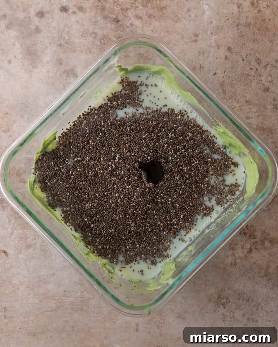 Chia seeds are being added to the green matcha milk mixture in a bowl, preparing for the chilling process of the chia pudding.
