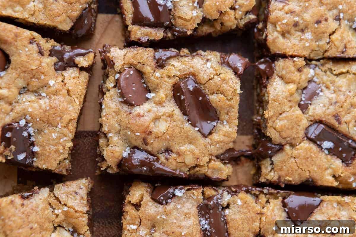 Overhead view of sliced oatmeal chocolate chip cookie bars with melted chocolate chunks and flaky salt on a wooden board