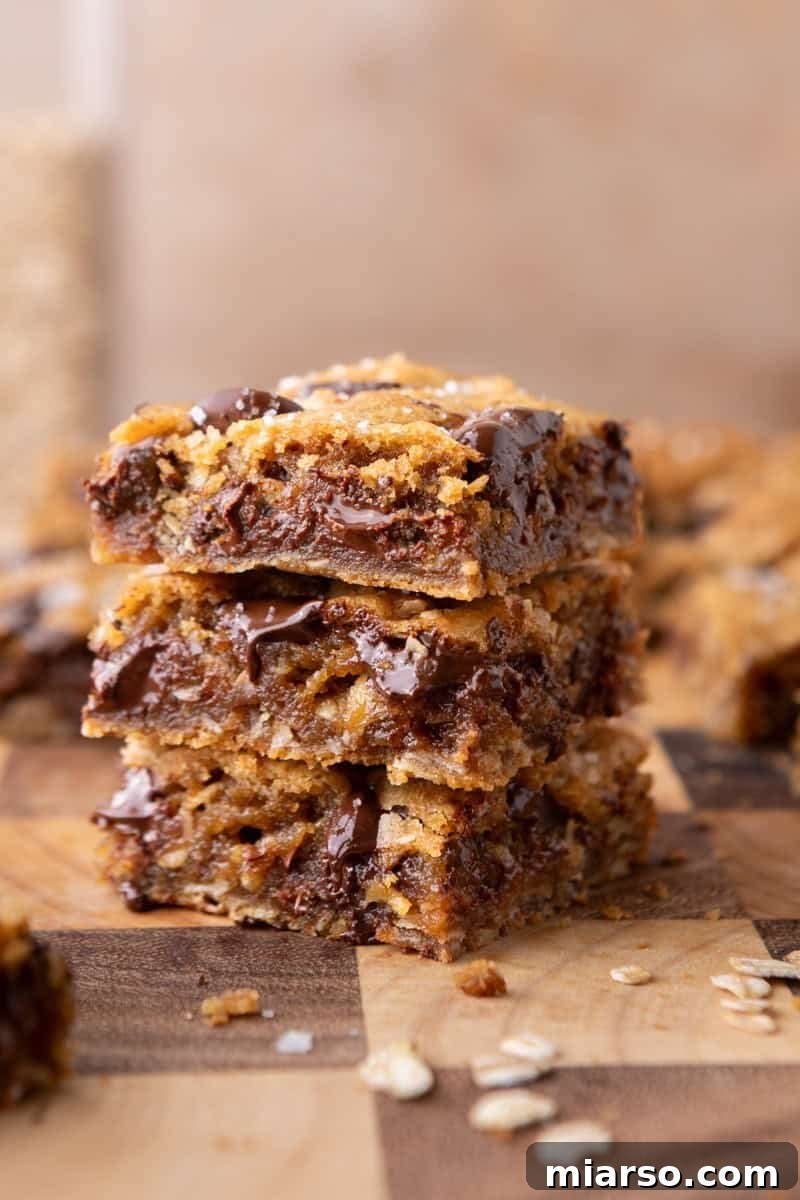 A stack of three thick brown butter oat bars with visible chocolate chunks and scattered oats on a wooden board