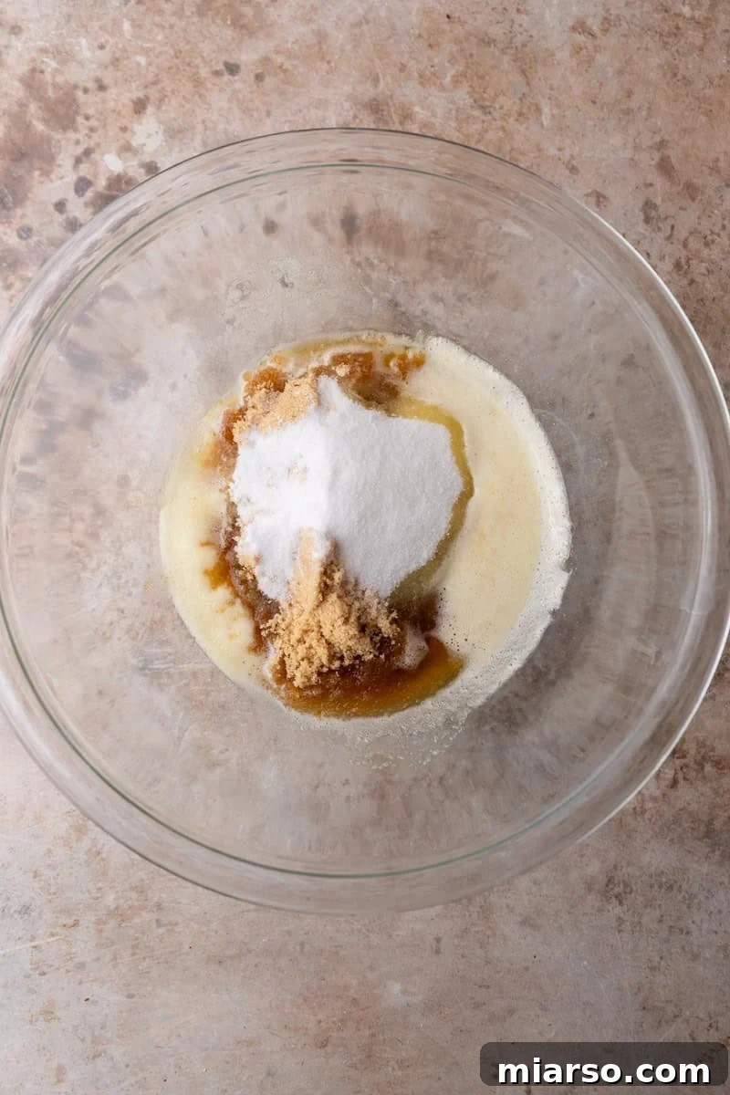 Brown butter with brown sugar and granulated sugar in a glass mixing bowl before whisking