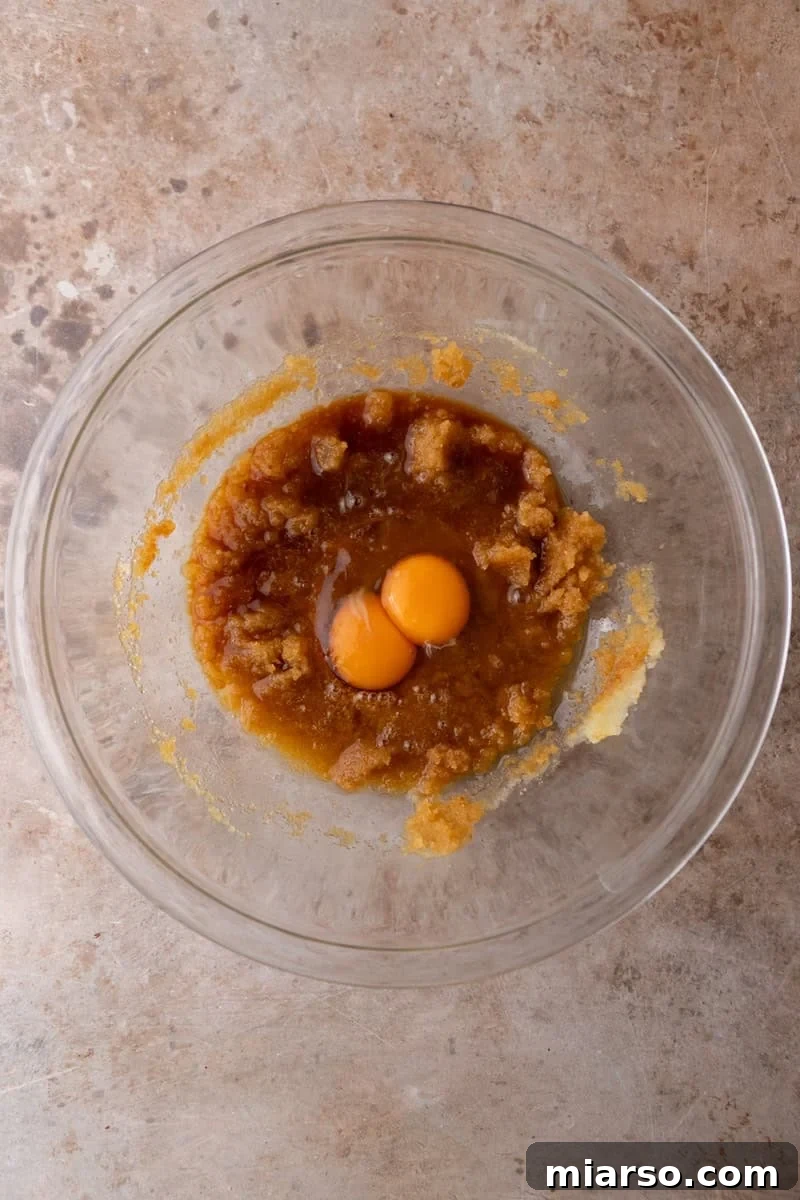 An egg and egg yolk added to a whisked brown butter and sugar mixture in a glass bowl
