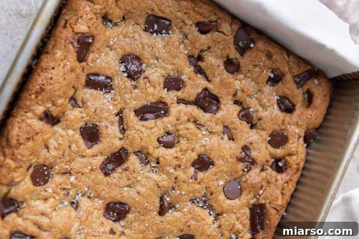 Freshly baked oatmeal cookie bar slab in a parchment-lined 8x8 baking pan topped with flaky salt