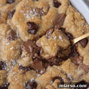 Scoopable chocolate chip cookie with molten chocolate center being scooped from a baking dish