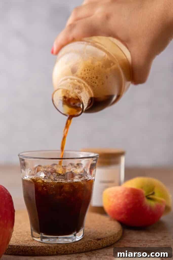 Pouring homemade Starbucks apple crisp oatmilk shaken espresso from a cocktail shaker over ice with fresh apples